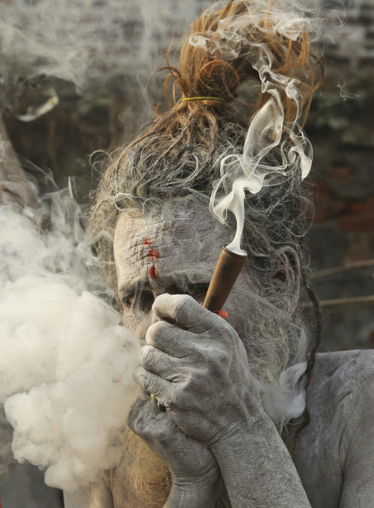 Aghori ascetic with ash-covered skin smoking rolled tobacco ritual with swirling smoke wallpaper