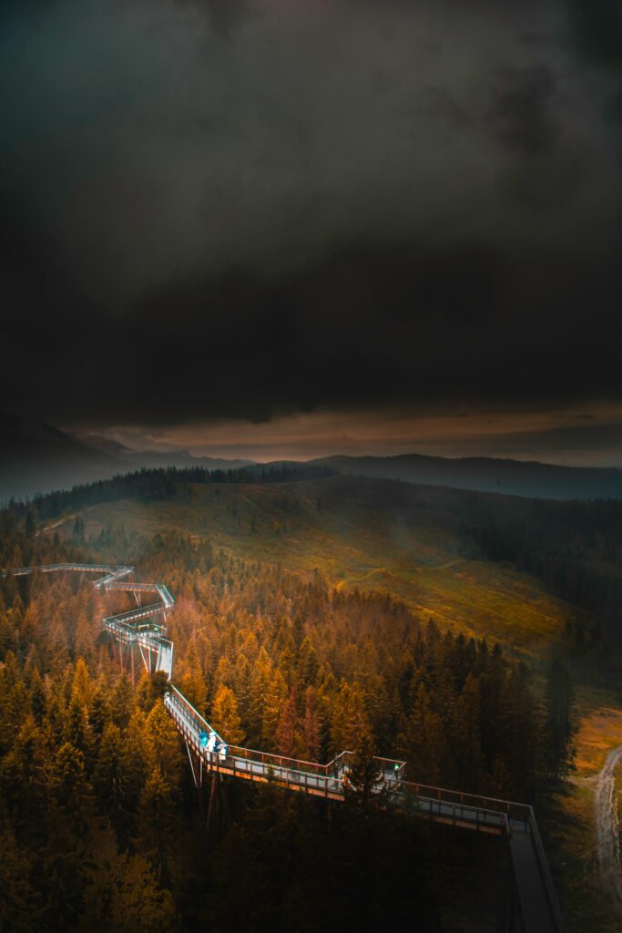 Aerial view of winding bridge over autumn forest with foggy mountains and dark cloudy sky Wallpaper