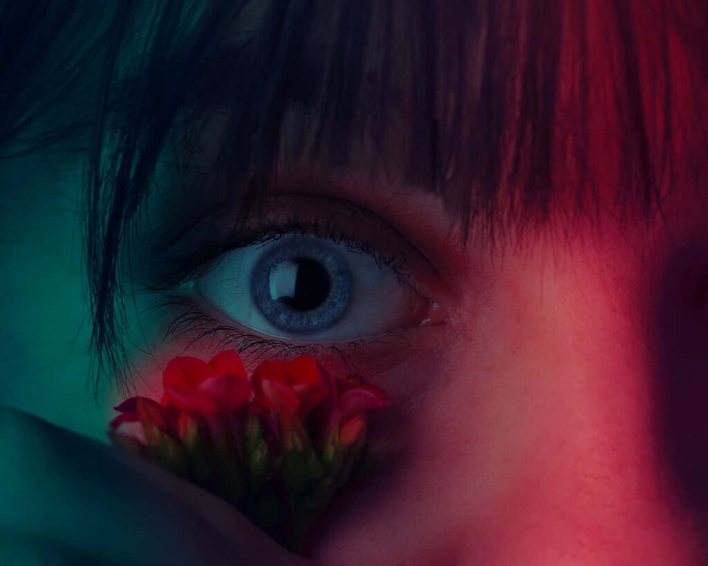Closeup of blue eye with red and green lighting and delicate red flowers dramatic wallpaper background