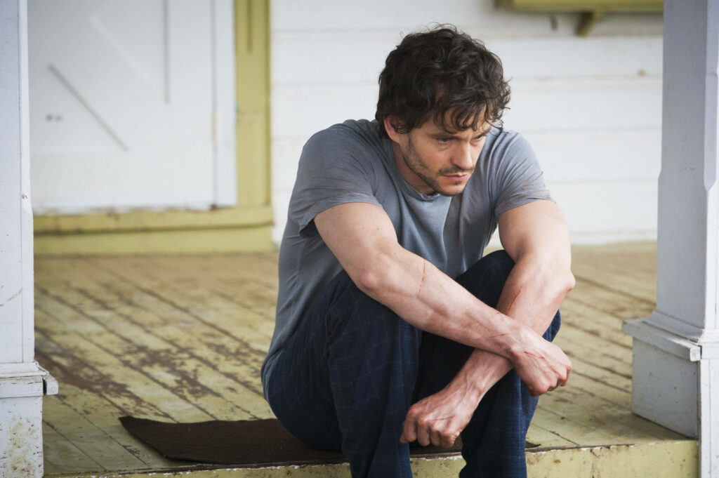 Mysterious Introspection: Man on Rustic Porch Wallpaper Background