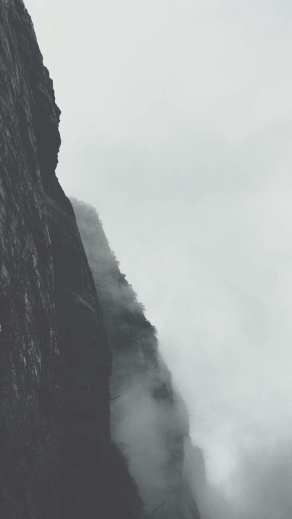 Enigmatic Monochrome Landscape: iPhone Snapshot of Cloud-Covered Mountain Cliff, Steeped in Gloomy Ambiance Wallpaper