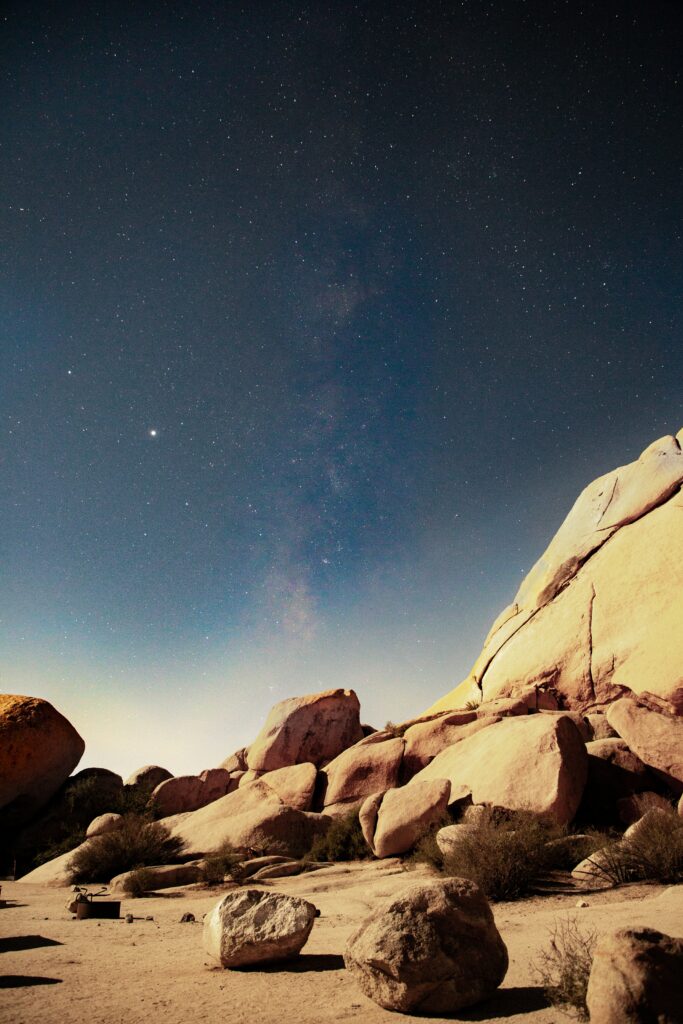 Moonlit desert stones and rugged rocks under a starry sky with a subtle nebula background wallpaper
