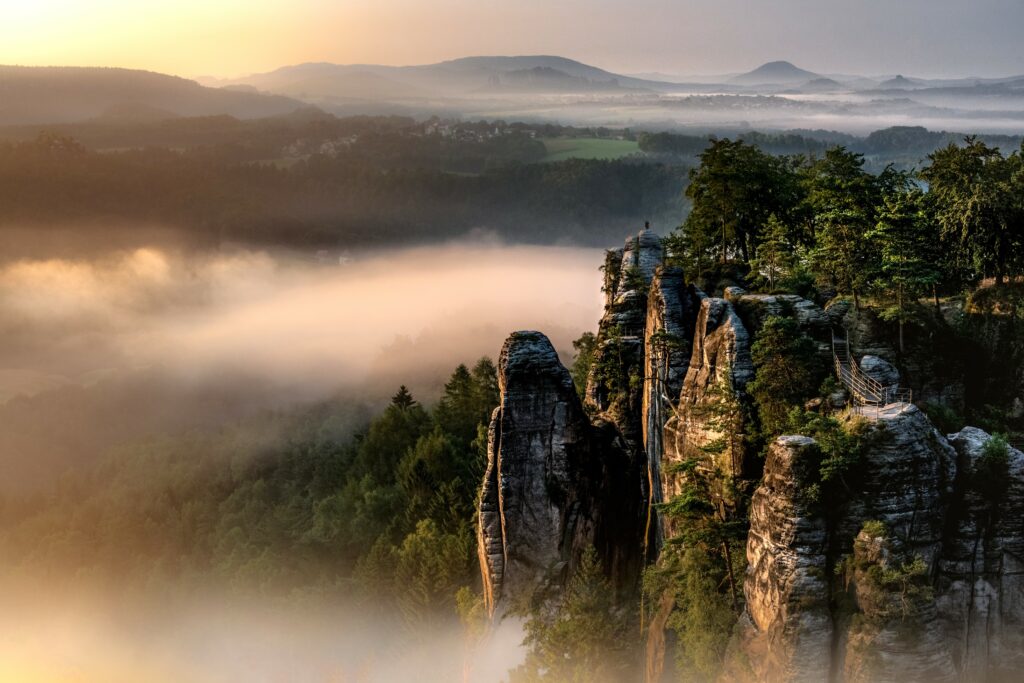 Morning fog over lush green forests and dramatic rock formations in a tranquil wilderness landscape Wallpaper