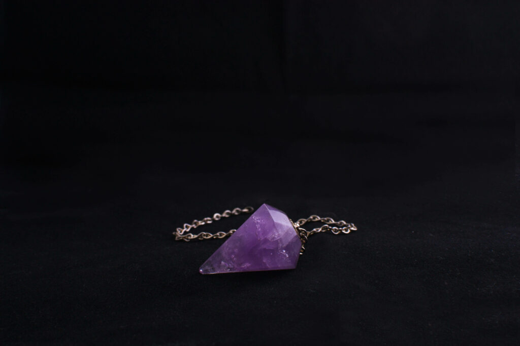 Polished amethyst pendulum on delicate chain resting on smooth black surface mystical wallpaper