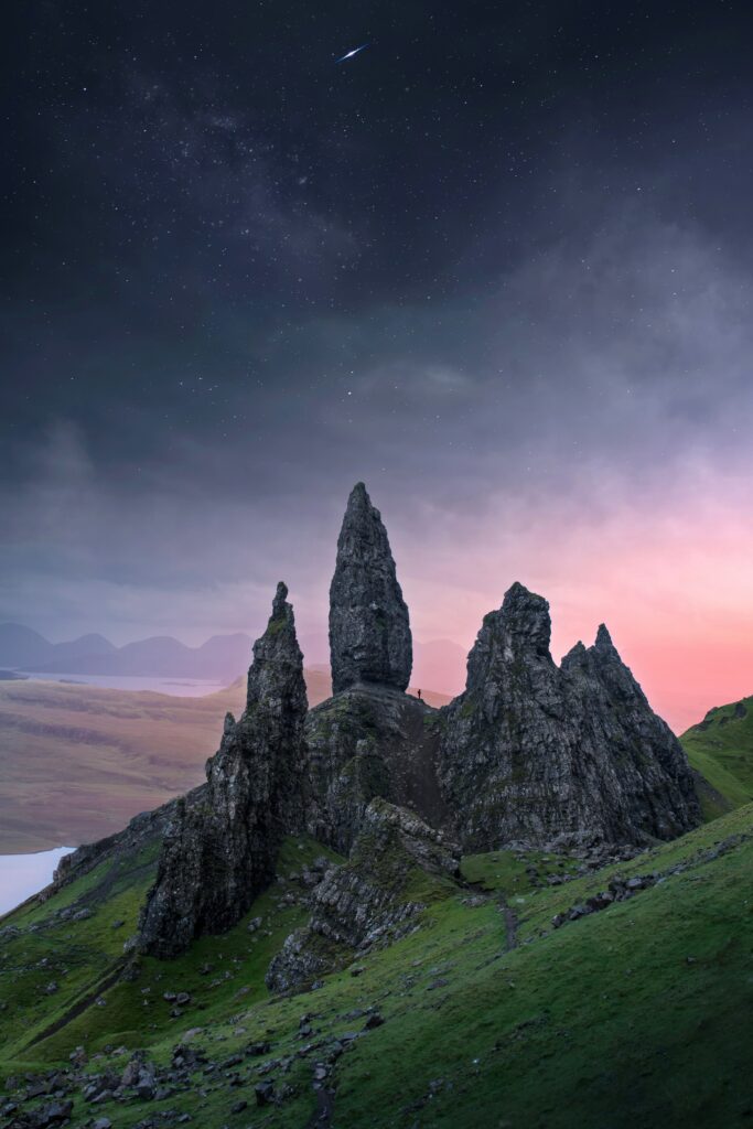 Dramatic rocky spires over lush green mountains at twilight with shooting star and pink indigo sky Wallpaper