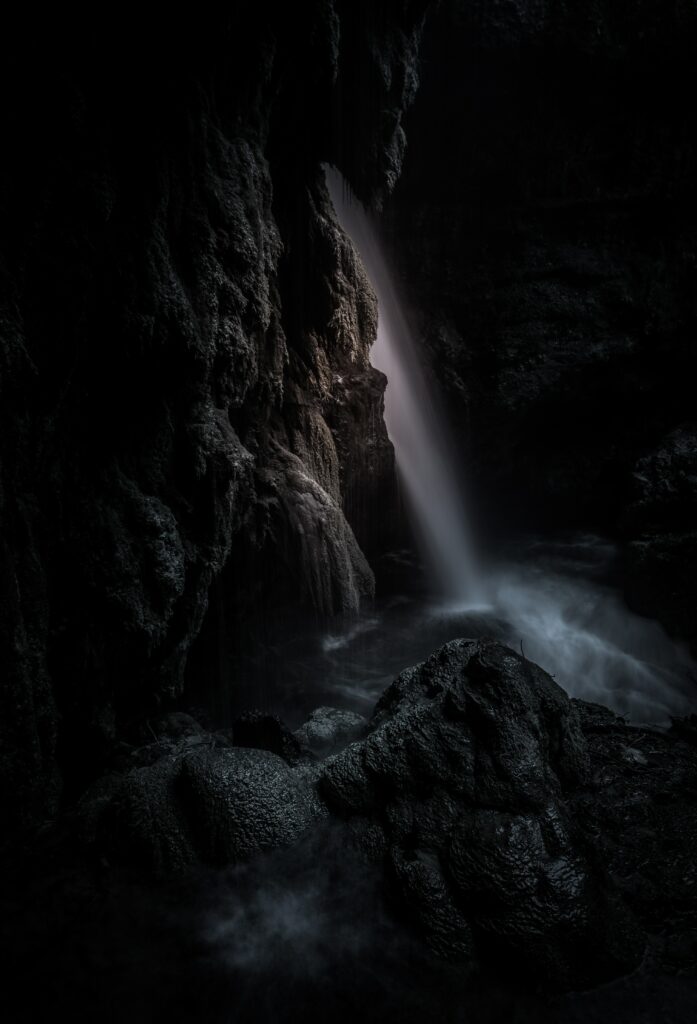 Mystical waterfall cascading through jagged rocks in a shadowy cave with soft mist and light Wallpaper