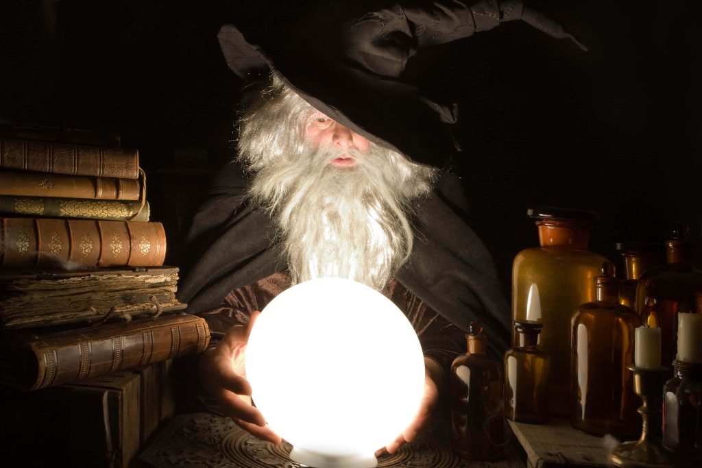 Bearded wizard in pointed hat gazing into glowing crystal ball with vintage books and bottles Wallpaper