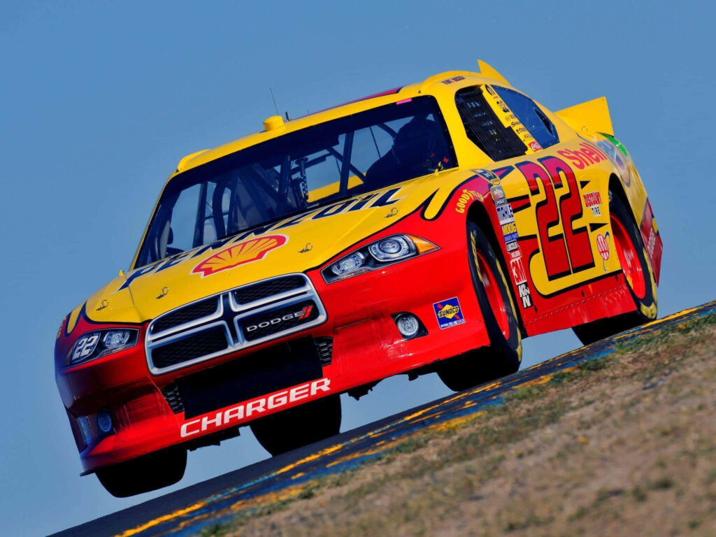 Yellow and red Dodge Charger speeding on NASCAR track vibrant motorsports wallpaper background