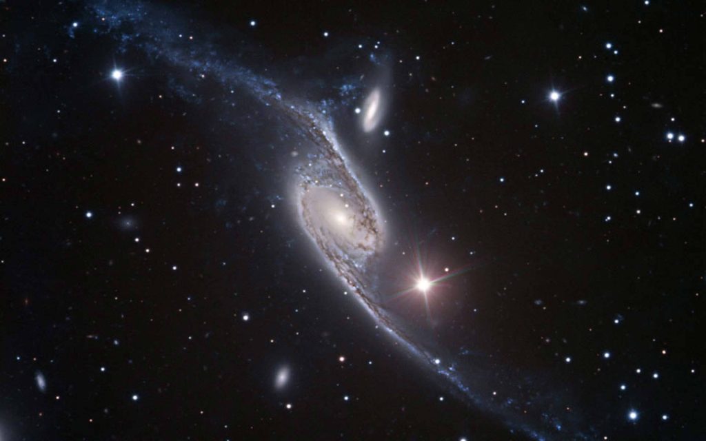 Twisted spiral galaxy NGC 3718 with glowing core and dust lanes against starry space background Wallpaper
