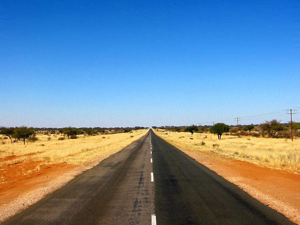 Namibia's Serene Desert Landscape: A Sunlit Oasis Along an Abandoned Concrete Path Wallpaper