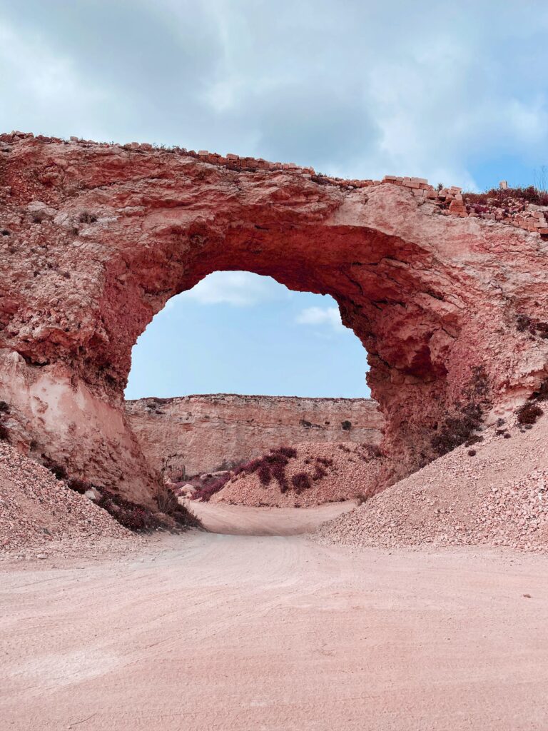 Natural rock arch in canyon with rugged textures warm earthy tones and soft blue sky background Wallpaper