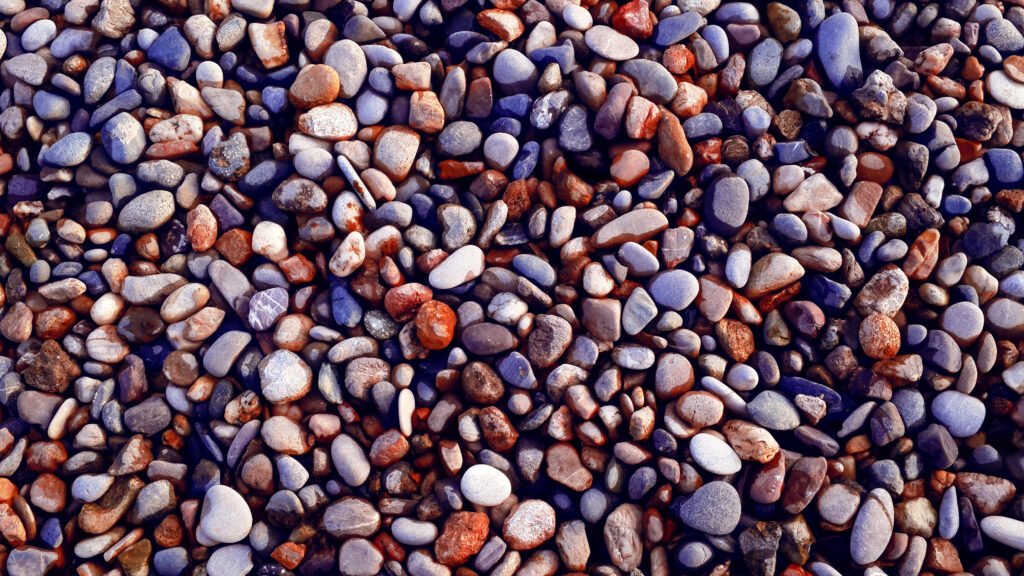 Close-up of smooth gray brown and muted purple stones and gravel natural textured wallpaper background