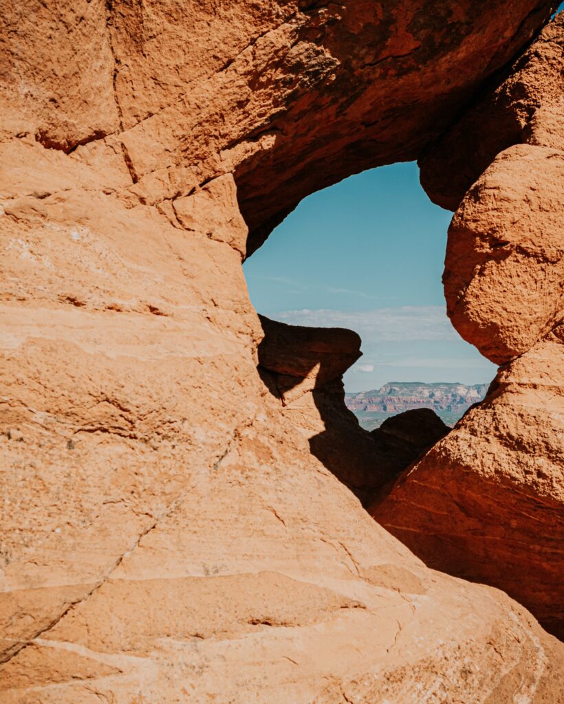 Natural stone arch of rugged orange rocks framing blue sky and distant canyon landscape wallpaper