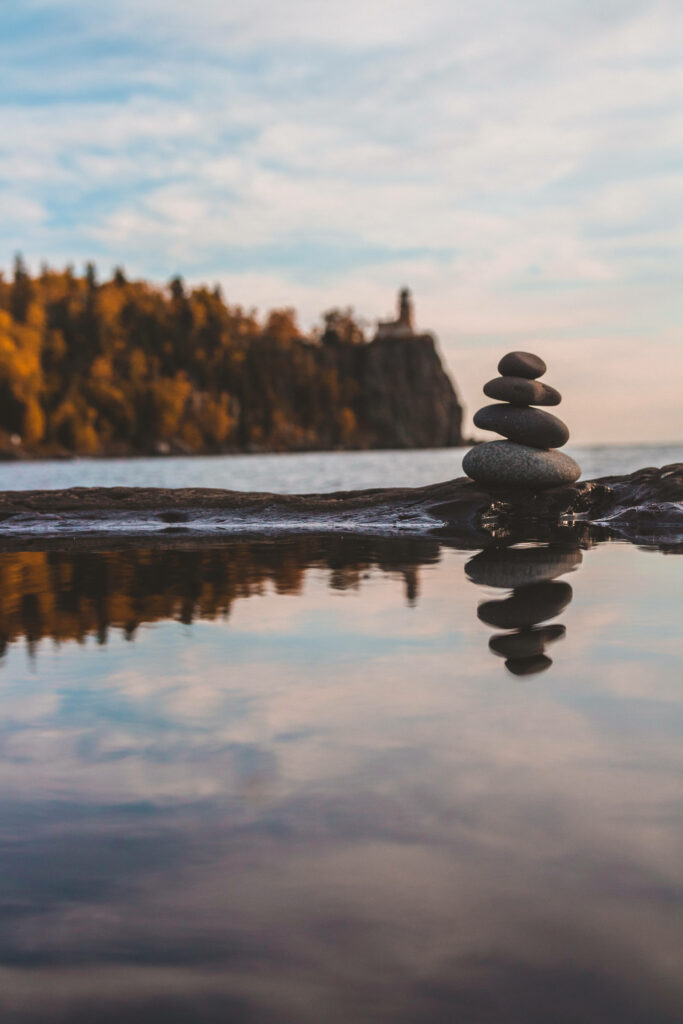Nature's Balance: Serene Autumn Reflections of Stacked Lake Rocks Amidst Trees - Phone Wallpaper