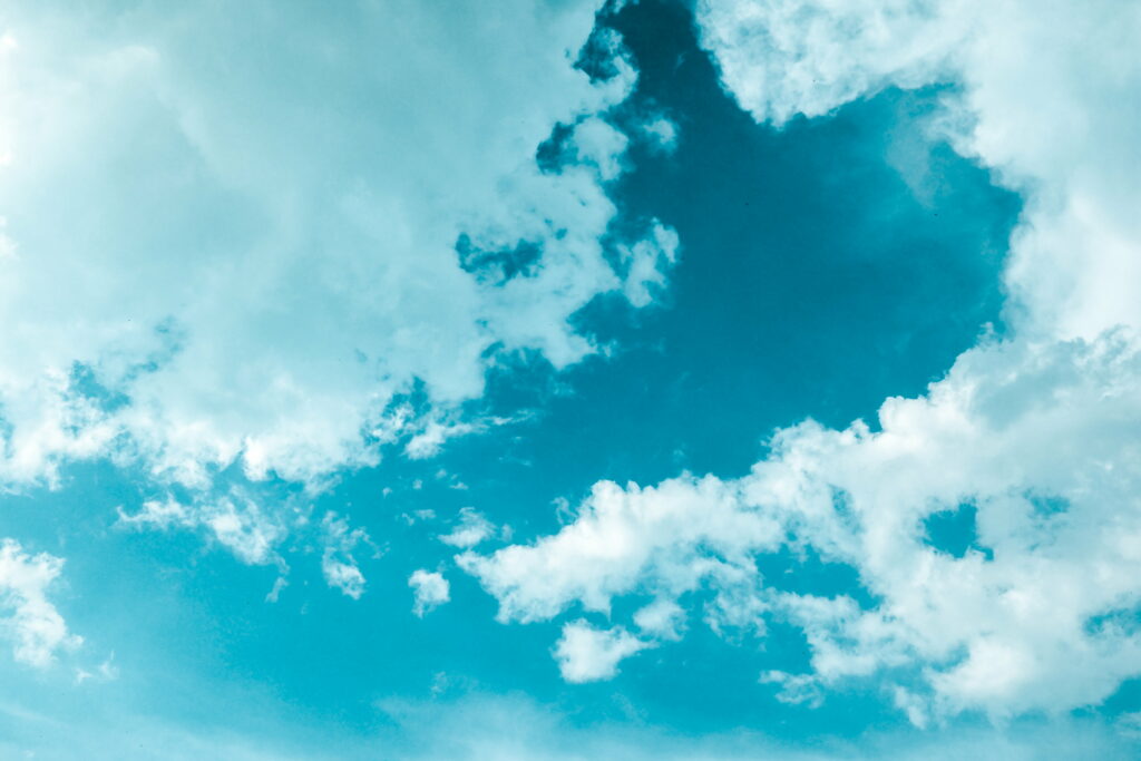 Fluffy white clouds drifting across a vibrant teal sky serene nature wallpaper background