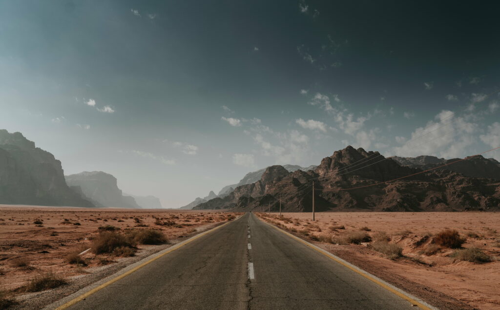 Empty asphalt highway leading to rocky mountains under deep blue sky Wadi Rum desert road wallpaper