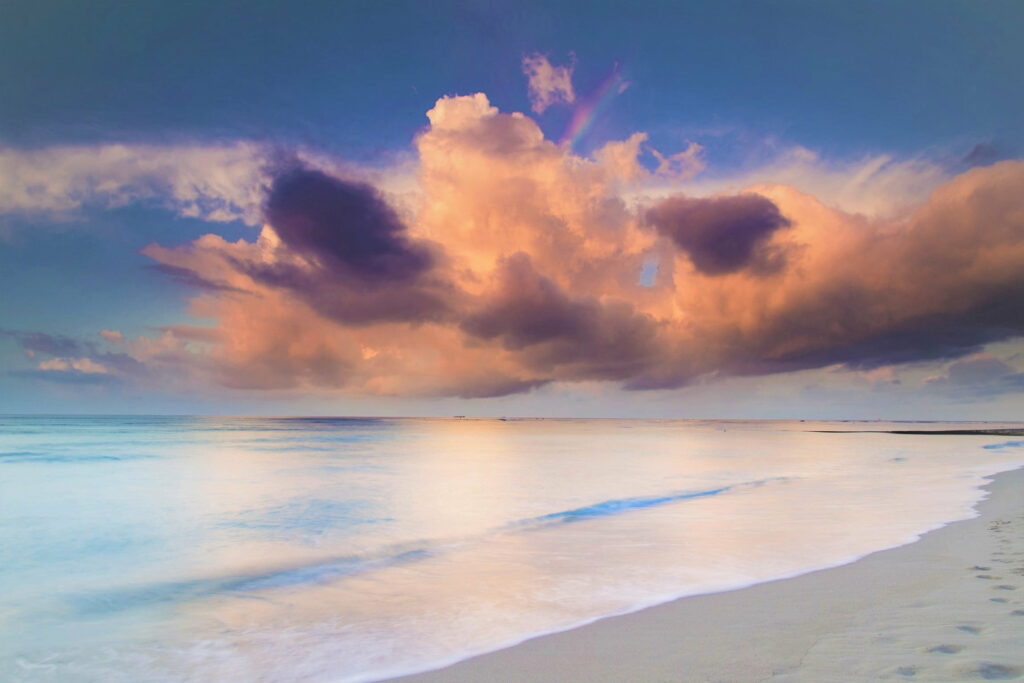 Serene golden hour shoreline with glowing clouds over calm reflective ocean pastel tones wallpaper