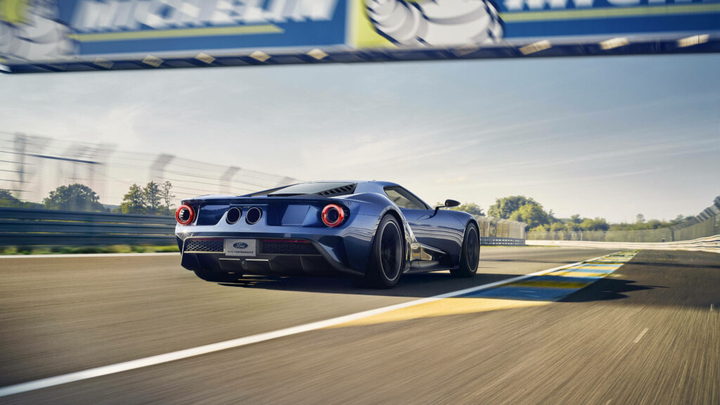 Navy blue Ford GT speeding on racetrack under sunny sky high performance sports car wallpaper