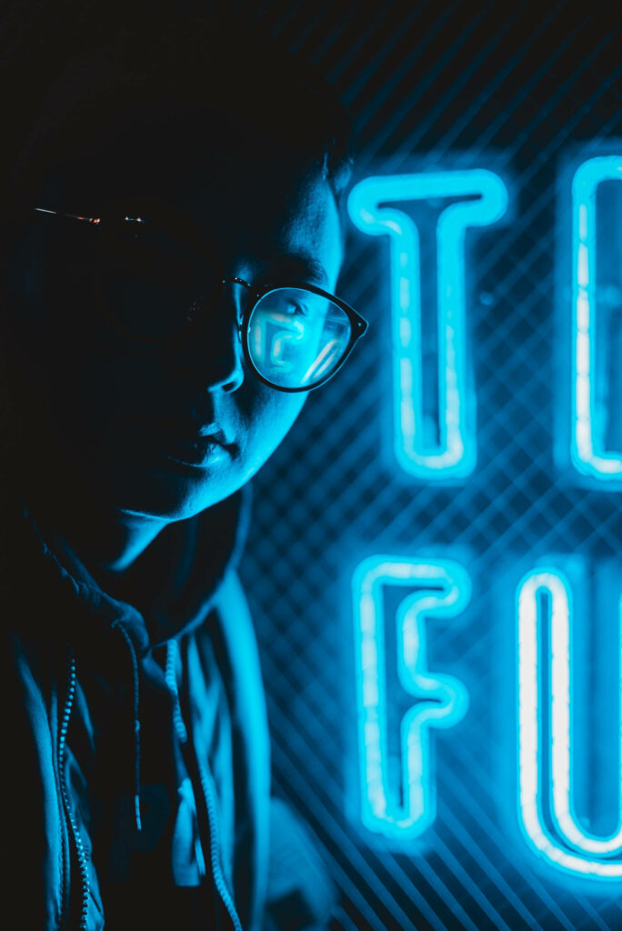 The Stylish Cyber Chic: Neon Blue iPhone Wallpaper featuring a Hooded Icon with Glasses amid Luminous Lettering