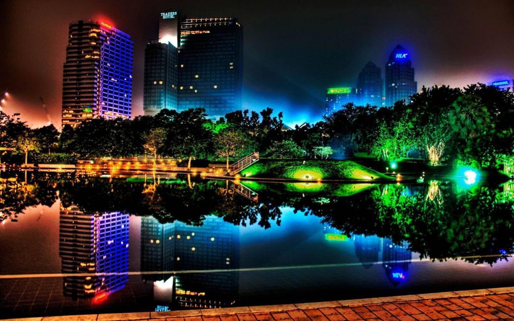 Neon Kuala Lumpur skyline at night with Traders Hotel and glowing trees reflected in lake Wallpaper