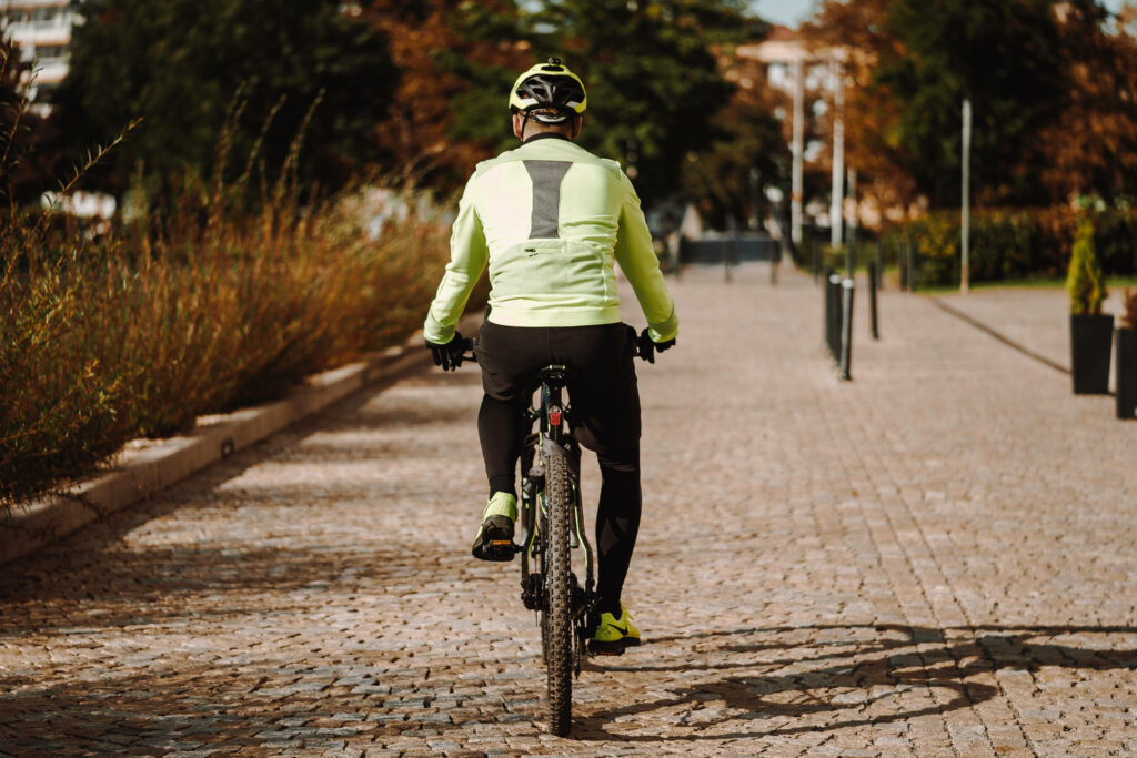 Cyclist in neon gear rides mountain bike on sunlit concrete path with autumn trees background Wallpaper