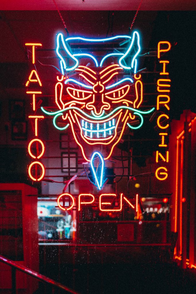 Neon glowing devil mask sign with tattoo piercing and open text in dark urban night background Wallpaper
