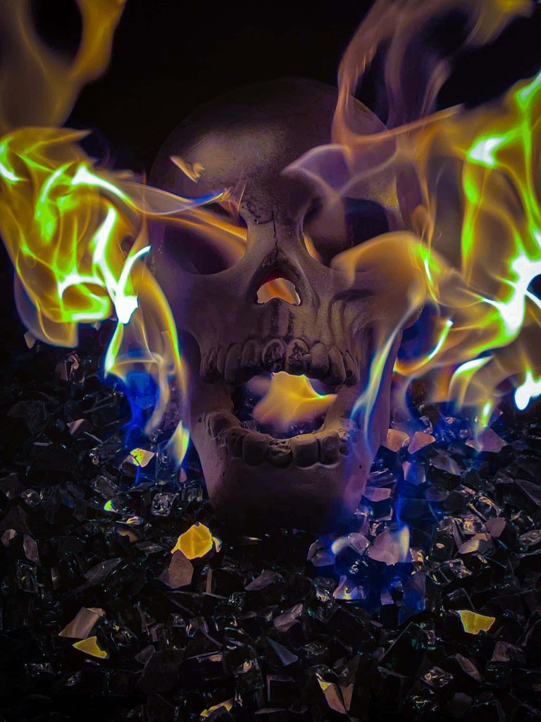 Flaming skull with neon green yellow flames on dark reflective glass shards gothic wallpaper