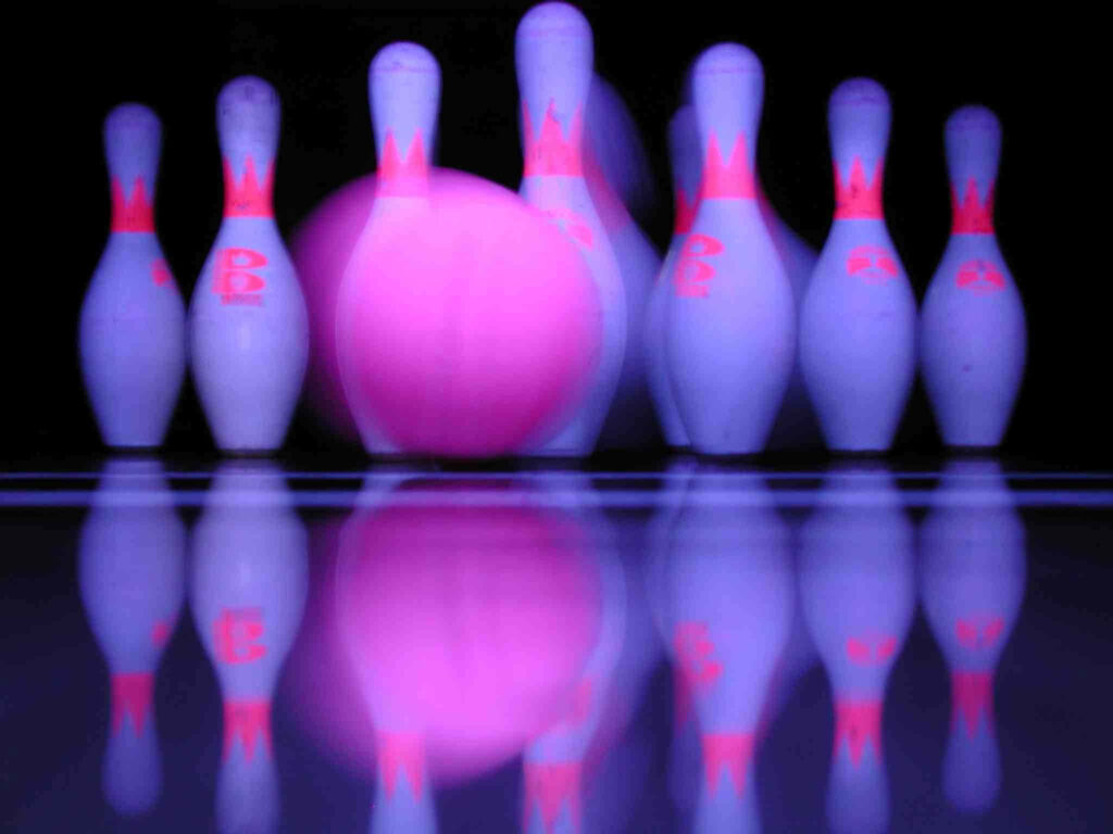 Vibrant neon pink bowling ball striking illuminated white pins in dynamic modern alley background Wallpaper