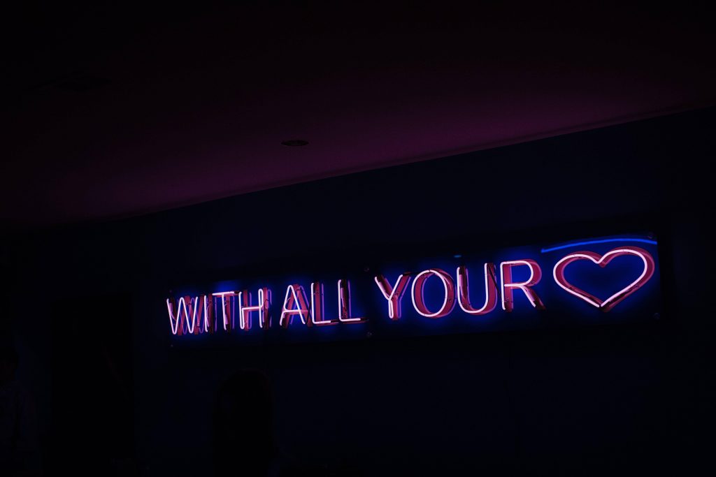 Neon pink glowing heart sign with the phrase with all your on dark moody background wallpaper