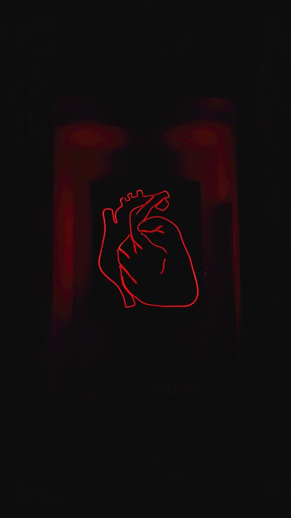 Neon red anatomical heart glowing on dark background with All Too Well text wallpaper design
