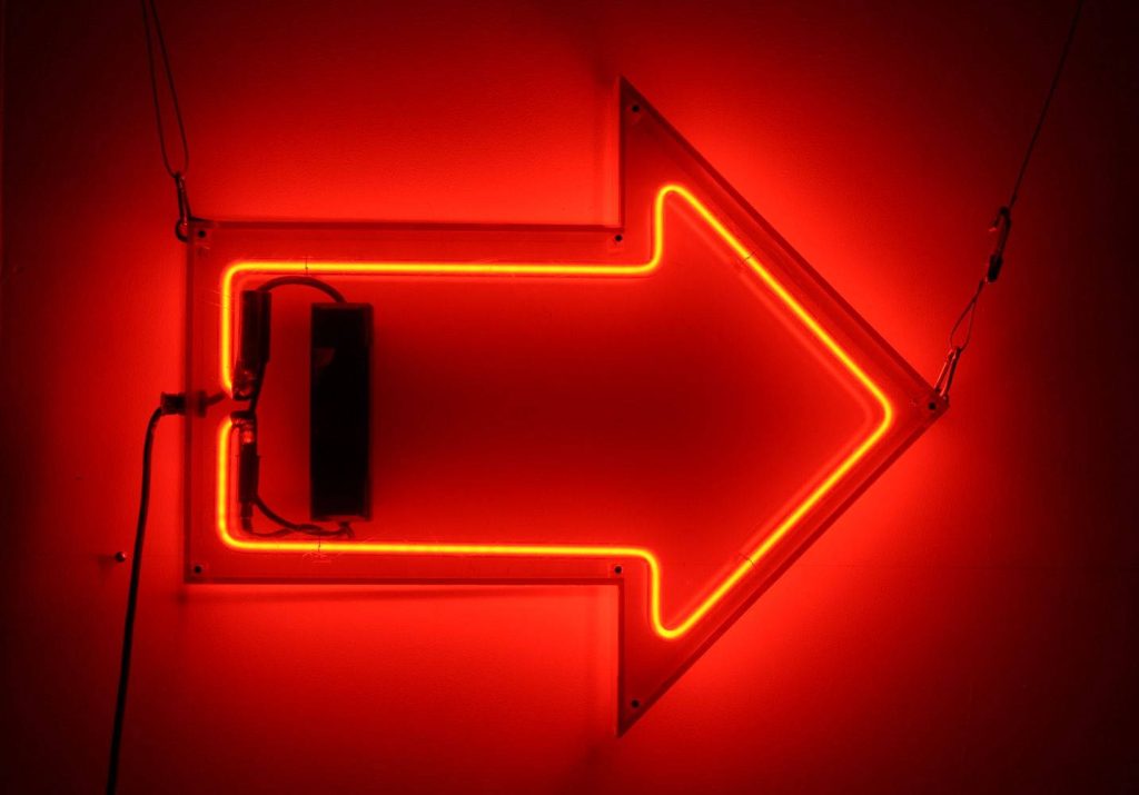 Glowing neon red directional arrow on minimal dark background edgy modern wallpaper design