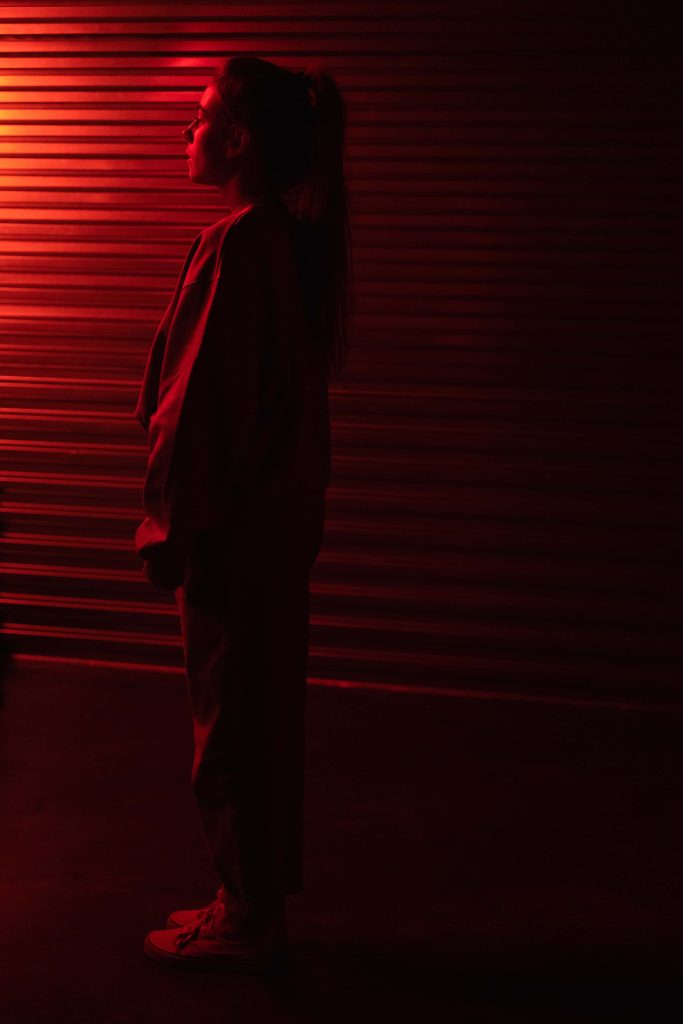 Girl in profile with neon red rim lighting against corrugated metal urban background wallpaper