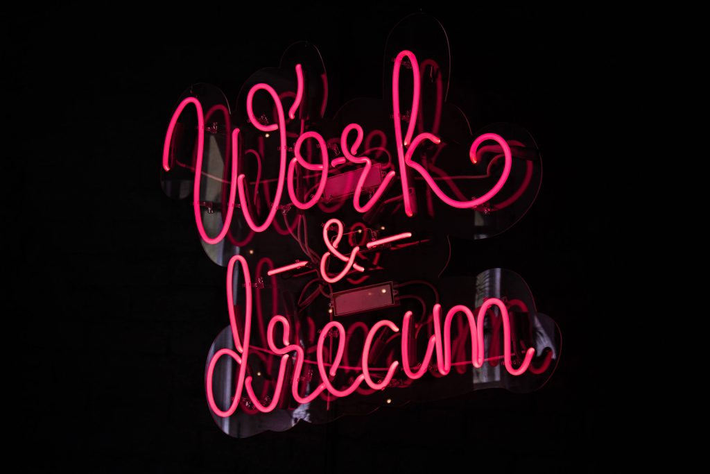Neon pink Work Dream sign glowing on dark minimalist wallpaper for modern inspirational desktop