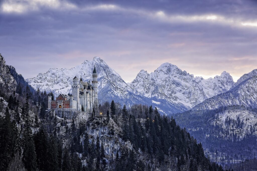 Neuschwanstein Castle in Bavaria on a hill with evergreen forests and snowy Alpine mountains Wallpaper
