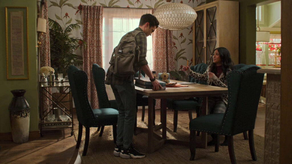 Darren Barnet and Maitreyi Ramakrishnan in sunlit stylish dining room scene from Never Have I Ever Wallpaper
