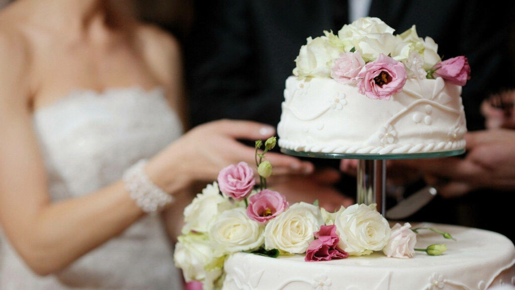 Newlyweds cutting floral wedding cake with white pink roses and delicate icing details background Wallpaper