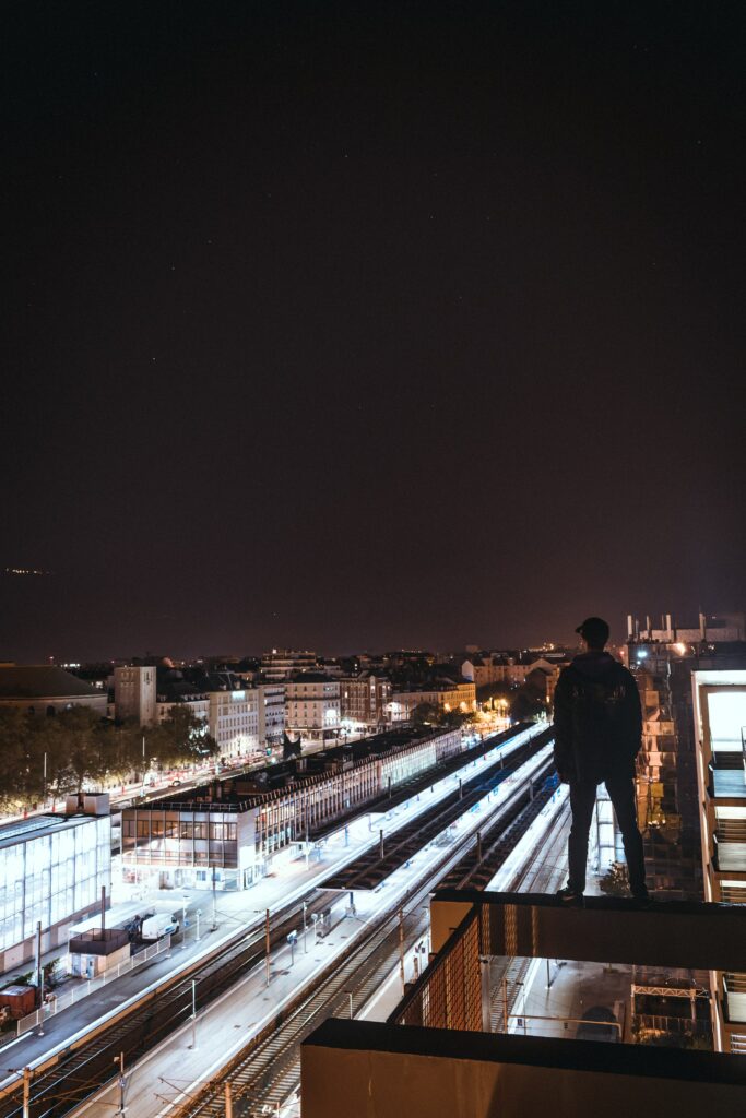 Moody Night Cityscape Wallpaper: Man on Rooftop with Lights