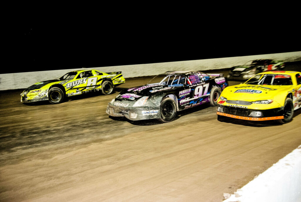 Three vibrant dirt race cars speeding on track at night showcasing motorsport action wallpaper