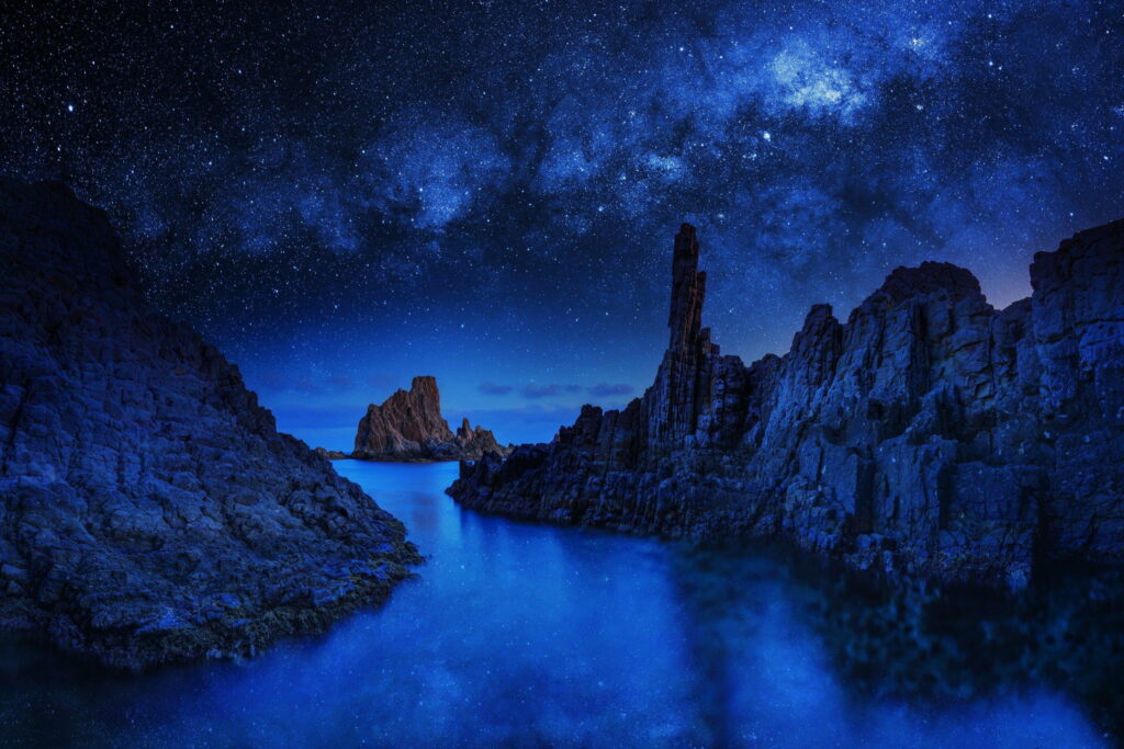 Nighttime Serenity: Stunning Ocean Rocks under a Starlit Blue Sky - Captivating HD Nature Wallpaper