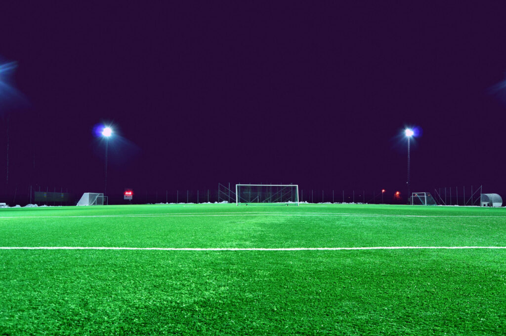 Nighttime Spectacle: Brilliantly Lit Green Football Haven under Starry Skies Wallpaper