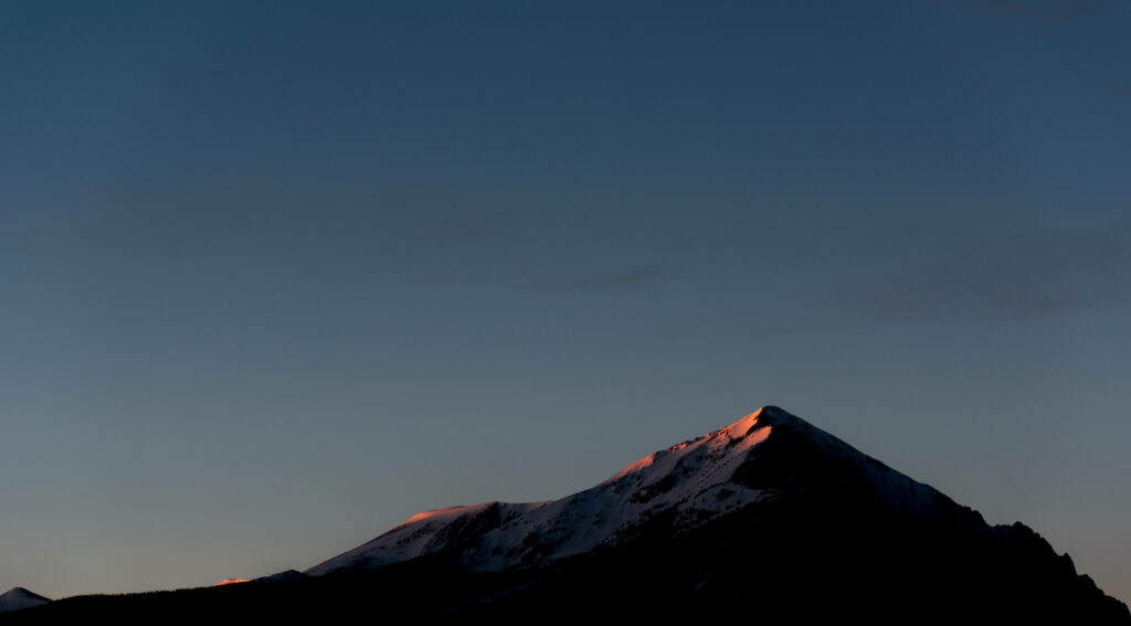 Snow-capped mountain peak with pink alpenglow and deep blue twilight sky minimalist wallpaper