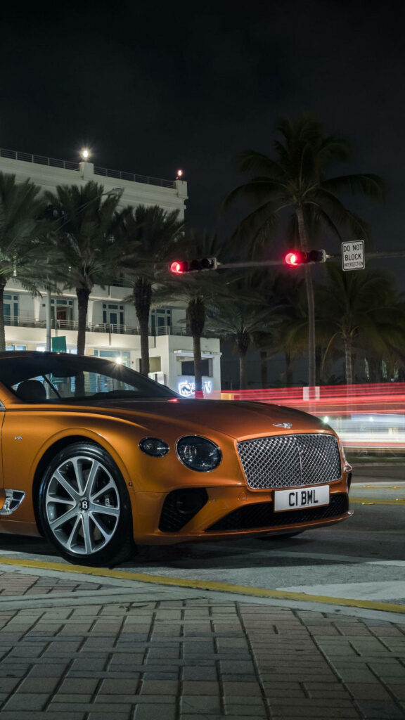 Nighthawk's Dream Ride: Orange Bentley Continental GT Shining on Stylish Permeable Pavements Wallpaper