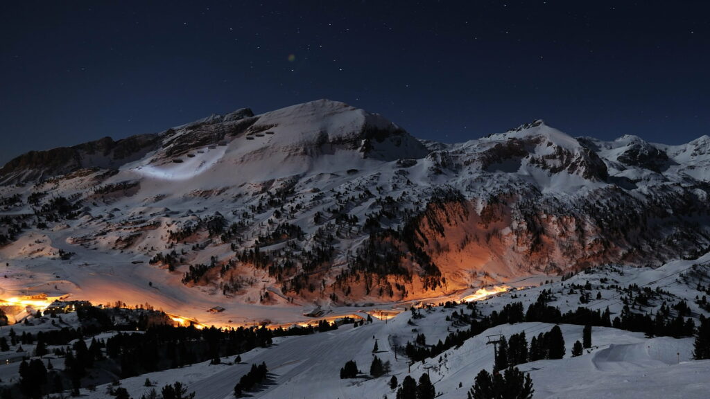 Snowy alpine mountains at night with warm lights under a starry winter sky wallpaper