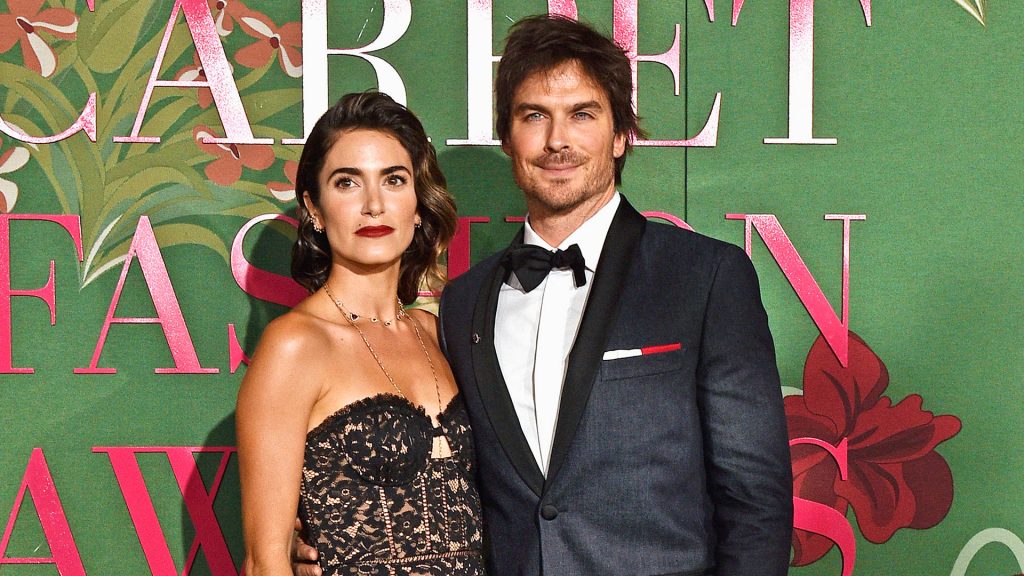 Nikki Reed in black lace gown with Ian Somerhalder in tuxedo on green floral red carpet backdrop Wallpaper