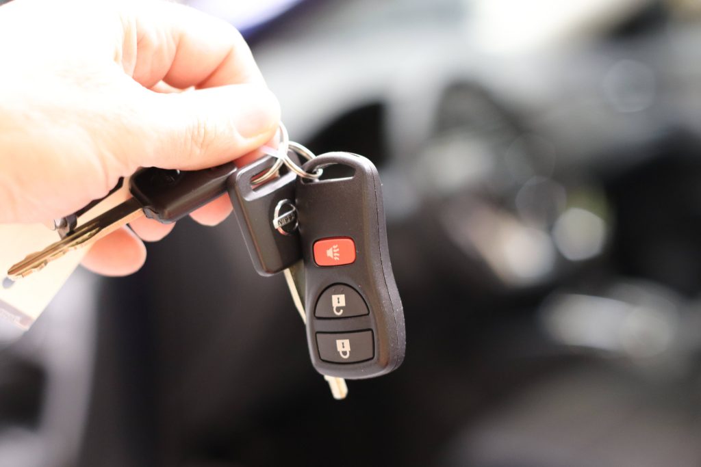 Close-up of Nissan car key fob with red panic button and lock controls on blurred interior background Wallpaper