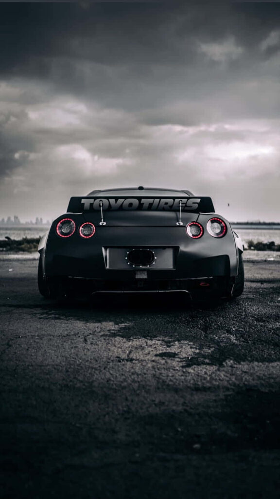 Monochrome Nissan GTR rear view with Toyo Tires city skyline cloudy sky iPhone wallpaper background