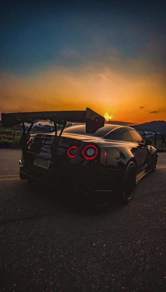 Sleek Nissan GTR with rear wing parked on open road at vibrant sunset perfect iPhone wallpaper