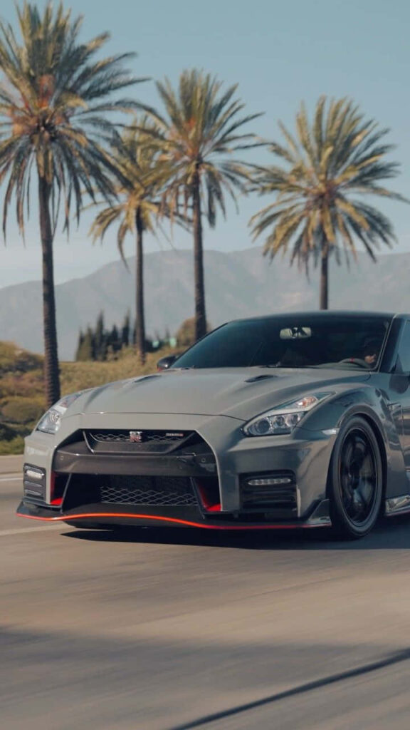 Nissan R35 GTR driving on sunlit palm tree road with mountains and clear blue sky background Wallpaper