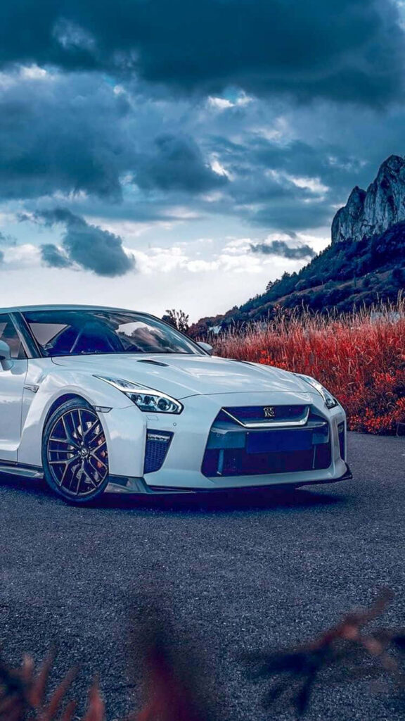 Nissan R35 GTR parked on winding road with dark clouds wild grass and rocky mountain backdrop Wallpaper