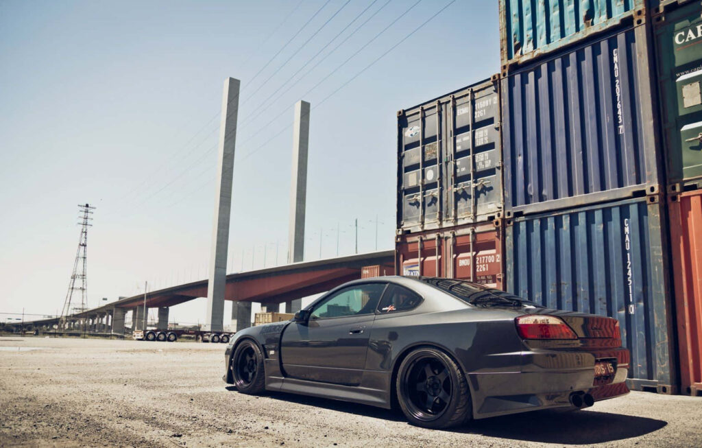 Sleek Nissan Silvia S15 with Ridge Widebody parked by colorful shipping containers industrial area Wallpaper